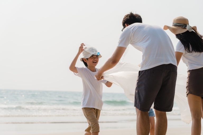 Asian young happy family activists collecting plastic waste on beach. Asia volunteers help to keep nature clean up and pick up garbage. Concept about environmental conservation pollution problems.